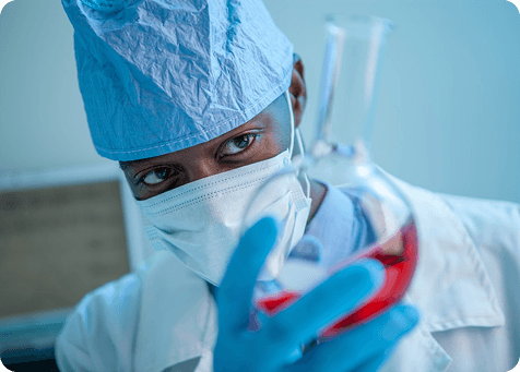 A lab worker in a mask holding a flask